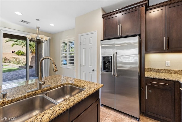 kitchen with visible vents, stainless steel fridge with ice dispenser, light stone counters, dark brown cabinets, and a sink