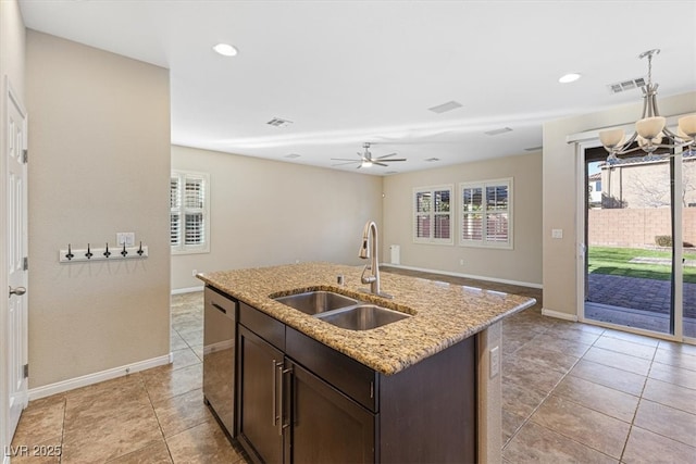 kitchen featuring a center island with sink, light stone counters, dark brown cabinets, pendant lighting, and a sink