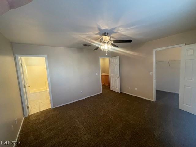 unfurnished bedroom with dark colored carpet, a spacious closet, ceiling fan, ensuite bath, and a closet