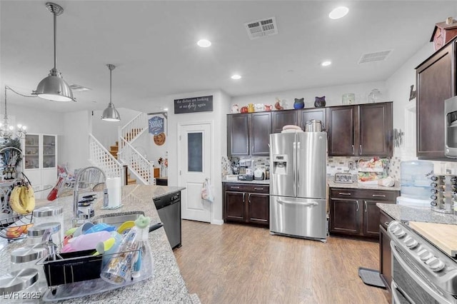 kitchen featuring appliances with stainless steel finishes, sink, hanging light fixtures, dark brown cabinetry, and light wood-type flooring