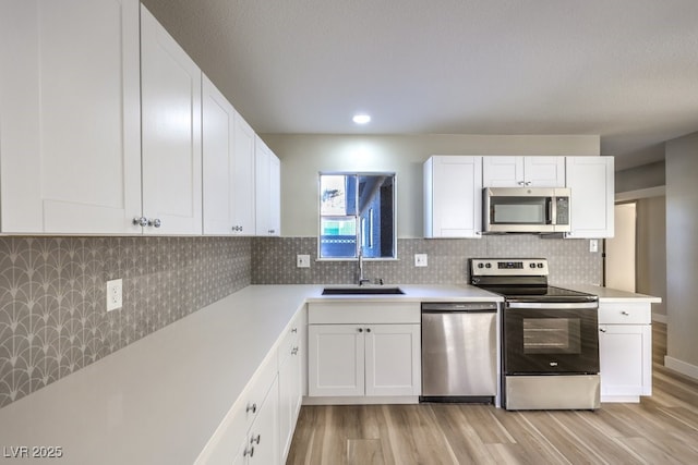 kitchen with white cabinets, light hardwood / wood-style floors, appliances with stainless steel finishes, and sink