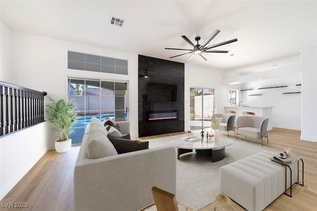 living room featuring ceiling fan, light wood-type flooring, and a high end fireplace