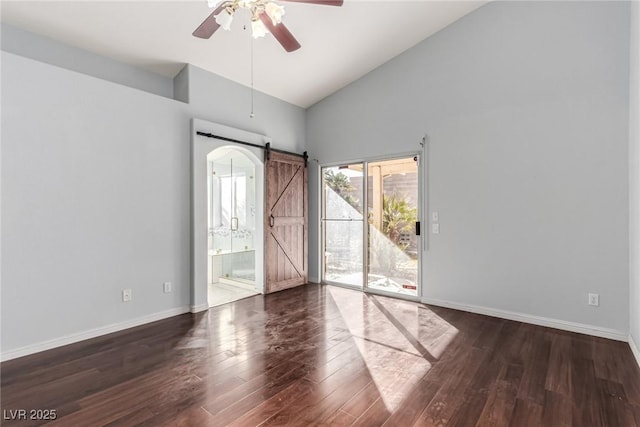 empty room with a barn door, dark hardwood / wood-style floors, high vaulted ceiling, and ceiling fan