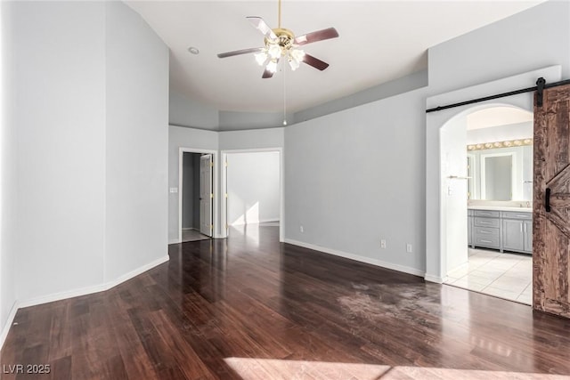 empty room with ceiling fan, a barn door, and light hardwood / wood-style floors