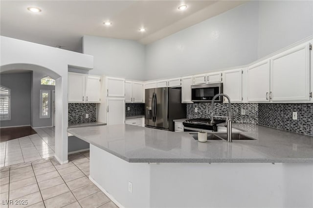 kitchen featuring black fridge, high vaulted ceiling, kitchen peninsula, light stone countertops, and white cabinets