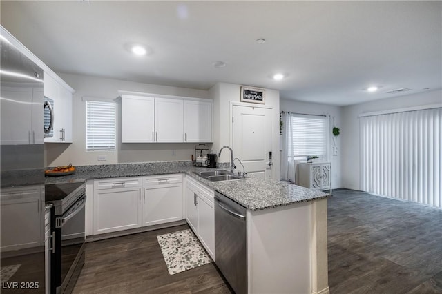 kitchen featuring dark wood finished floors, a peninsula, a sink, appliances with stainless steel finishes, and white cabinetry