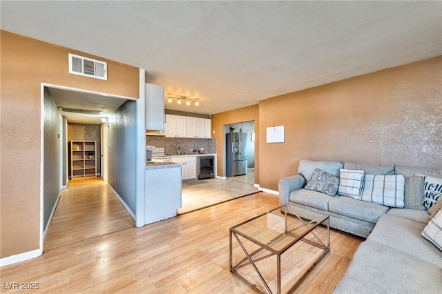 living room featuring wine cooler, rail lighting, and light wood-type flooring