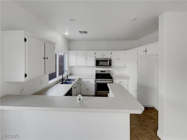 kitchen with white cabinetry, kitchen peninsula, stainless steel appliances, tile patterned floors, and sink