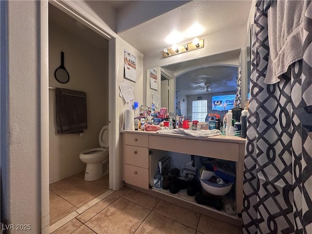 bathroom with tile patterned flooring, vanity, ceiling fan, toilet, and a textured ceiling