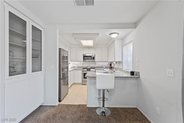 kitchen featuring sink, stainless steel appliances, white cabinets, light colored carpet, and kitchen peninsula