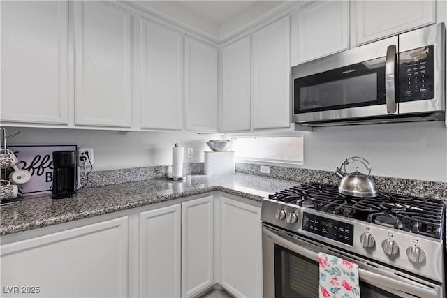 kitchen featuring white cabinetry, stainless steel appliances, and dark stone counters