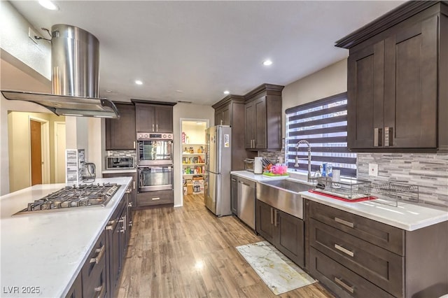 kitchen featuring sink, dark brown cabinets, island exhaust hood, stainless steel appliances, and light hardwood / wood-style floors