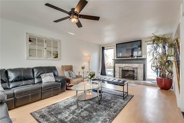 living room with ceiling fan, a high end fireplace, and light hardwood / wood-style floors