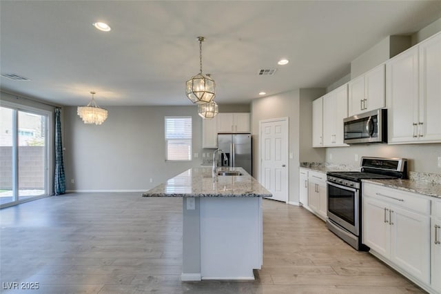 kitchen with appliances with stainless steel finishes, pendant lighting, white cabinetry, an island with sink, and light hardwood / wood-style floors