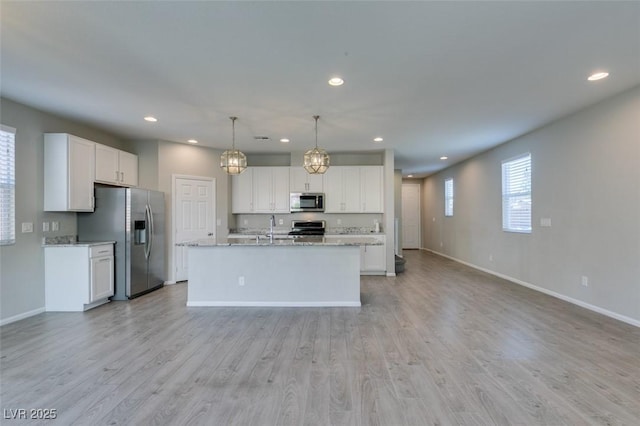 kitchen featuring stainless steel appliances, a kitchen island with sink, pendant lighting, and white cabinets