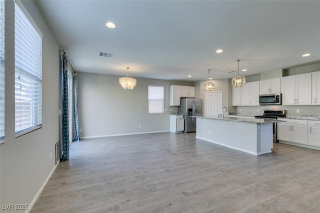 kitchen with white cabinetry, appliances with stainless steel finishes, a kitchen island with sink, and pendant lighting