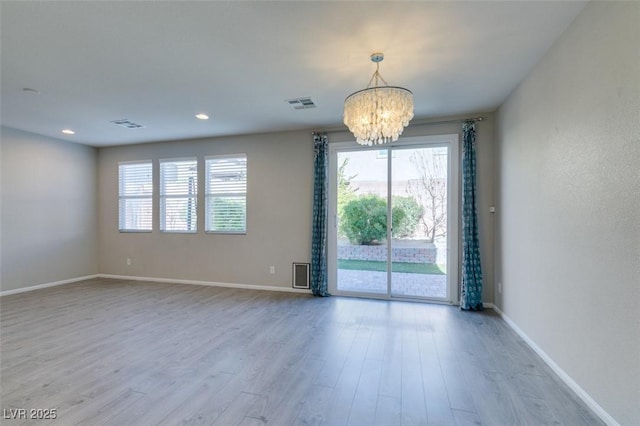 spare room featuring a notable chandelier and light hardwood / wood-style flooring