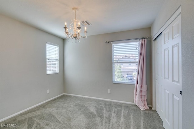 carpeted empty room featuring an inviting chandelier