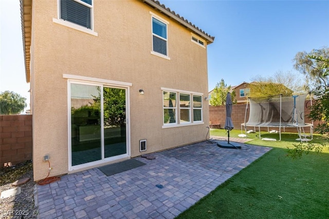 back of property featuring a yard, a patio area, and a trampoline