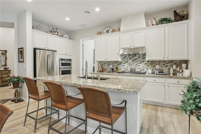 kitchen featuring under cabinet range hood, visible vents, a sink, white cabinetry, and stainless steel appliances