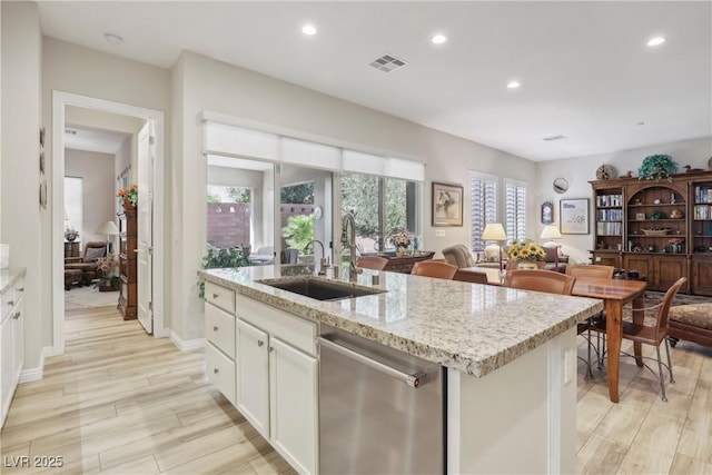 kitchen with light wood finished floors, a kitchen island with sink, recessed lighting, stainless steel dishwasher, and a sink