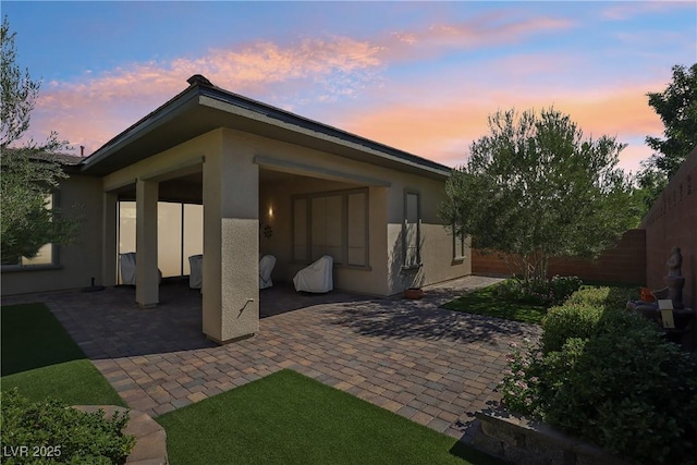 back of house at dusk featuring a patio, fence, and stucco siding