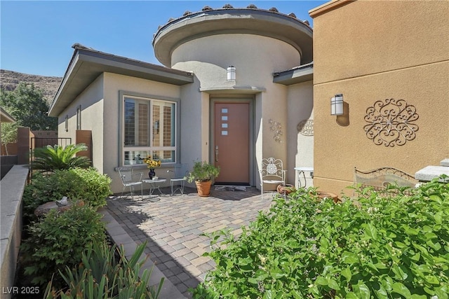 entrance to property featuring stucco siding, a patio, and fence