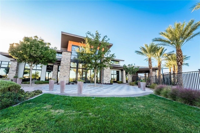 rear view of property featuring stucco siding, stone siding, a lawn, and fence