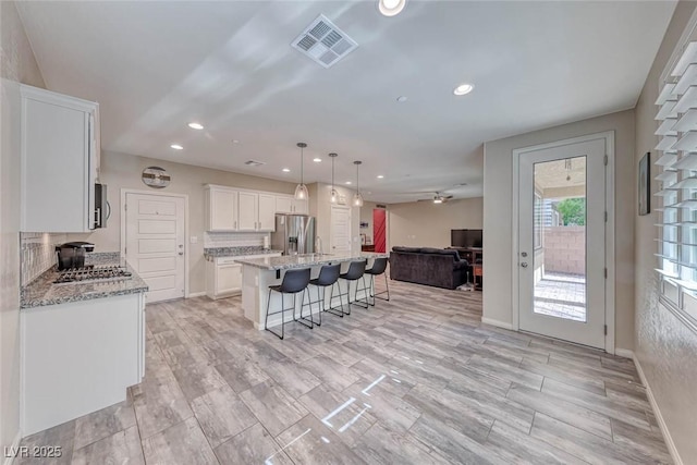 kitchen featuring a kitchen island, appliances with stainless steel finishes, white cabinetry, a breakfast bar area, and hanging light fixtures