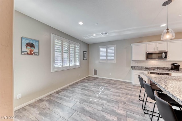 kitchen featuring appliances with stainless steel finishes, white cabinetry, backsplash, a kitchen bar, and light stone counters