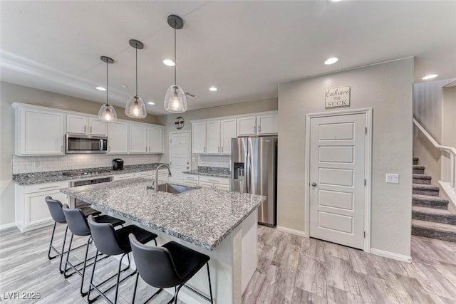 kitchen with sink, appliances with stainless steel finishes, white cabinetry, an island with sink, and decorative light fixtures