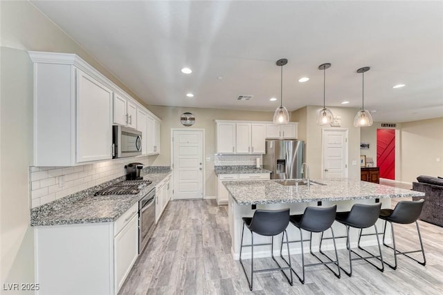 kitchen with appliances with stainless steel finishes, pendant lighting, white cabinetry, an island with sink, and sink