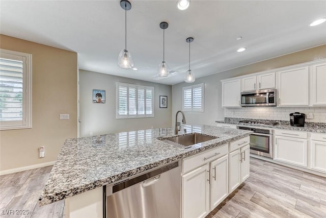 kitchen featuring stainless steel appliances, white cabinetry, sink, and a center island with sink