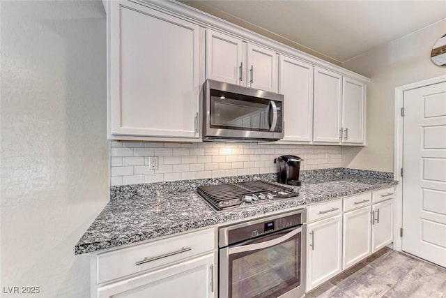 kitchen featuring stainless steel appliances, white cabinetry, dark stone counters, and decorative backsplash