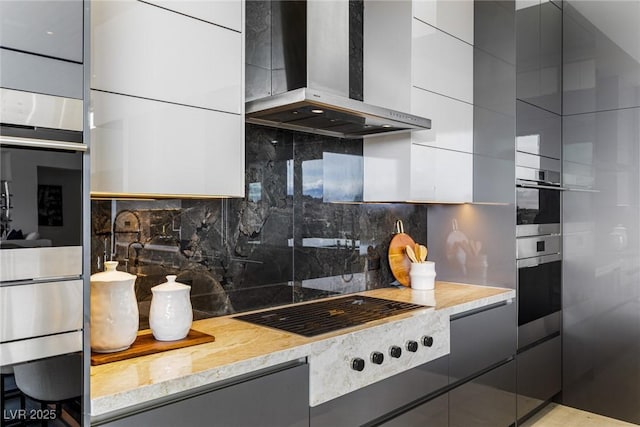 kitchen with gray cabinets, backsplash, black stovetop, light stone countertops, and wall chimney exhaust hood