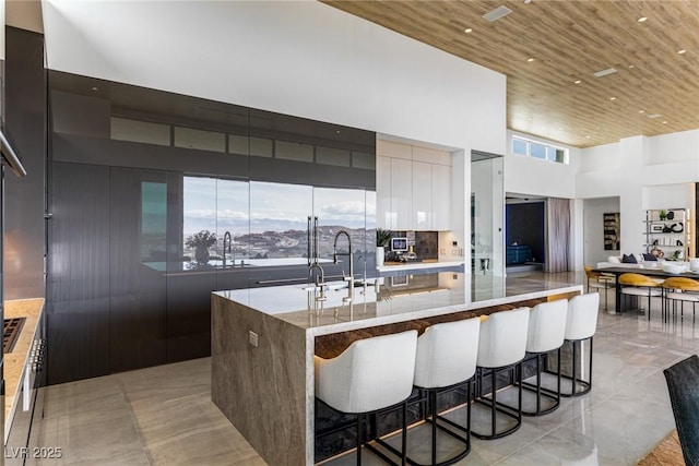 kitchen featuring wood ceiling, a towering ceiling, a breakfast bar, and a center island with sink