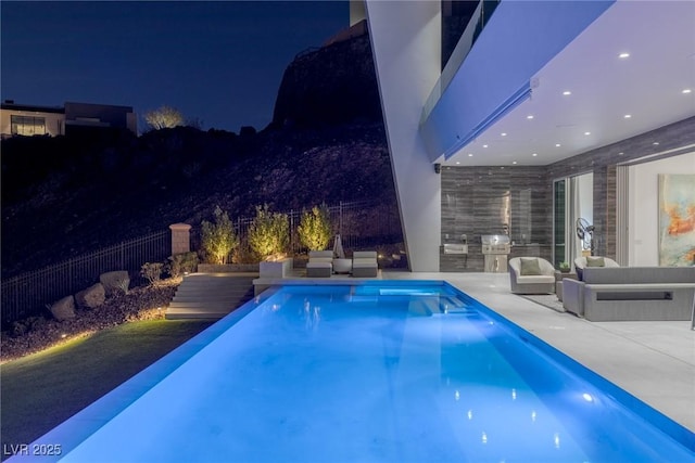 pool at night with an outdoor kitchen, an outdoor living space, and a patio area