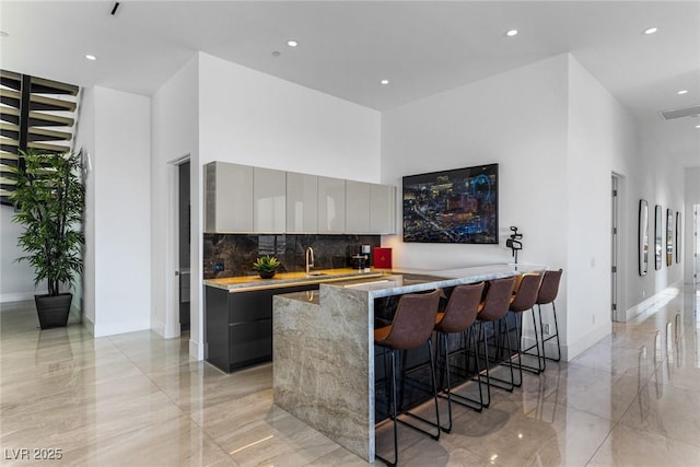 kitchen with a towering ceiling, gray cabinetry, a breakfast bar area, decorative backsplash, and kitchen peninsula