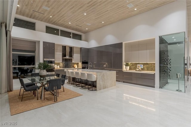 kitchen featuring wood ceiling, backsplash, a high ceiling, and wall chimney range hood