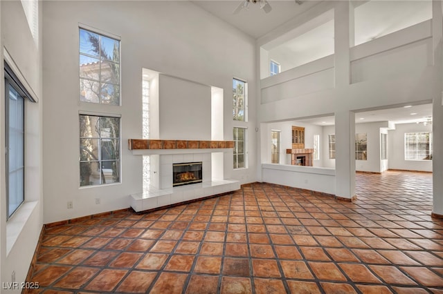 unfurnished living room featuring a tiled fireplace, a high ceiling, tile patterned floors, and ceiling fan