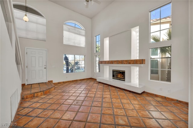 unfurnished living room featuring ceiling fan, a towering ceiling, tile patterned floors, and a tiled fireplace