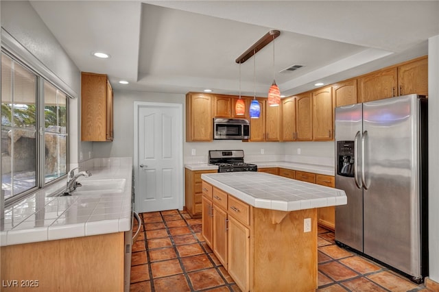 kitchen with stainless steel appliances, a raised ceiling, a kitchen island, and tile counters