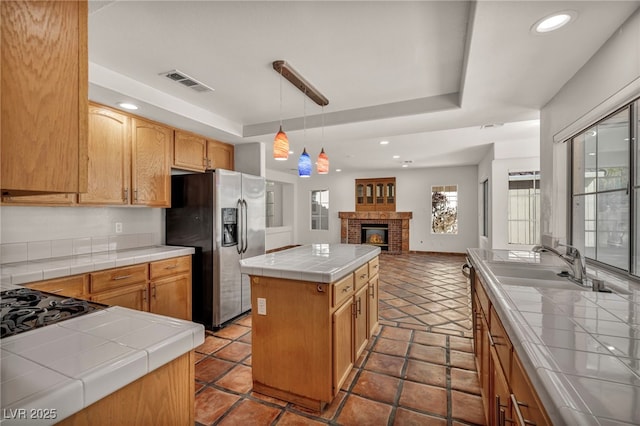 kitchen featuring stainless steel refrigerator with ice dispenser, a center island, tile countertops, and a tray ceiling