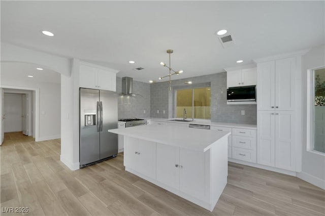 kitchen featuring wall chimney range hood, sink, appliances with stainless steel finishes, white cabinetry, and a center island