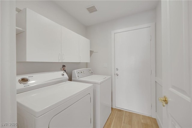 clothes washing area with cabinets, washing machine and clothes dryer, and light hardwood / wood-style floors