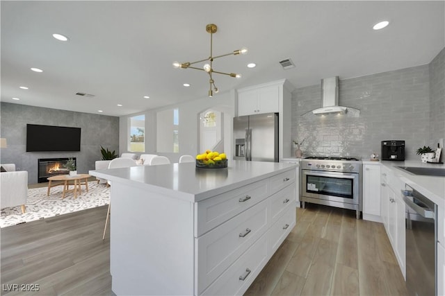 kitchen featuring white cabinetry, decorative light fixtures, light hardwood / wood-style floors, appliances with stainless steel finishes, and wall chimney exhaust hood