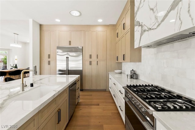 kitchen featuring sink, light stone counters, decorative light fixtures, light brown cabinets, and appliances with stainless steel finishes