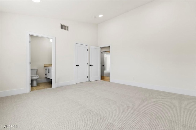 unfurnished bedroom with light carpet, connected bathroom, and a towering ceiling