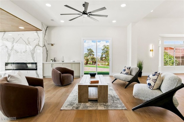 living room featuring ceiling fan, a fireplace, and light hardwood / wood-style flooring