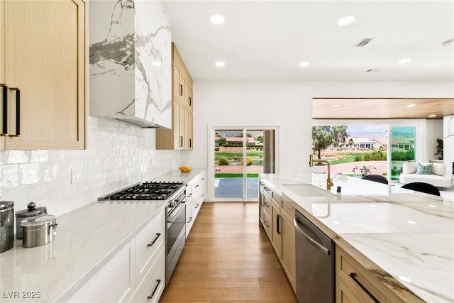 kitchen with sink, light stone counters, appliances with stainless steel finishes, light hardwood / wood-style floors, and decorative backsplash